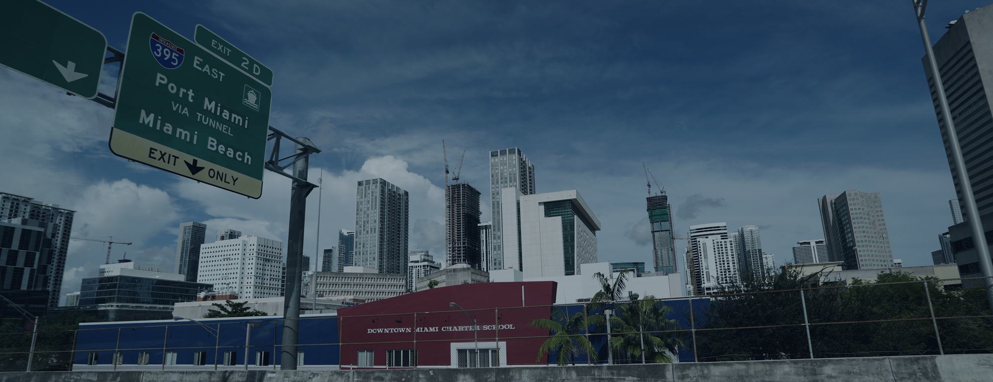 Downtown Miami skyline seen from the I-395 overpass, cranes above a charter school